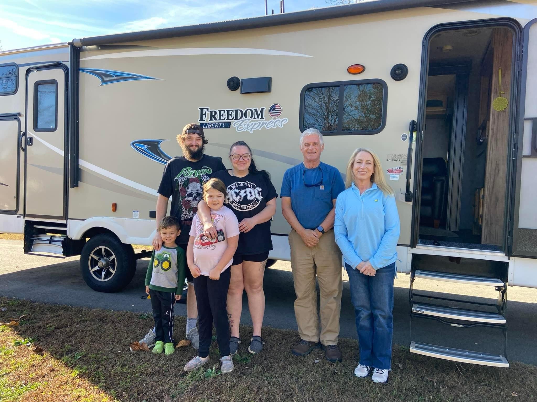 A group of adults and children standing beside a travel trailer in an EmergencyRV program photograph.
