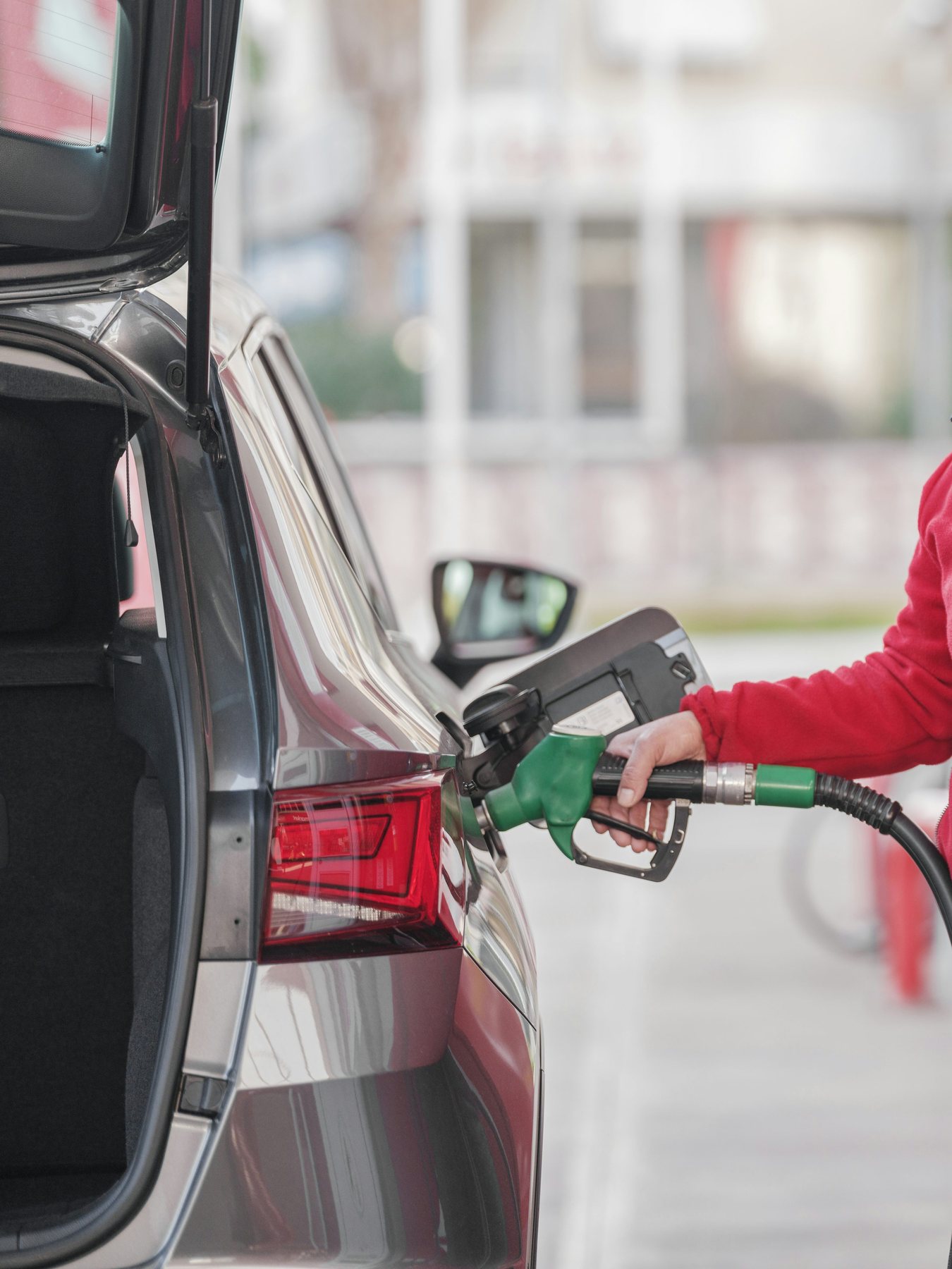 A hand holding a fuel nozzle while filling a vehicle’s tank.