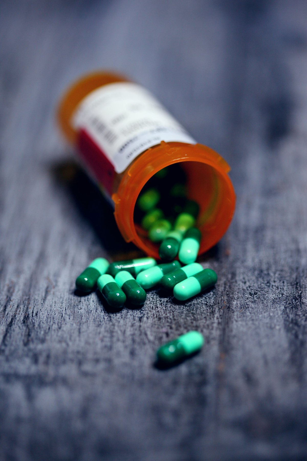 An orange prescription bottle with green capsules on a tabletop.