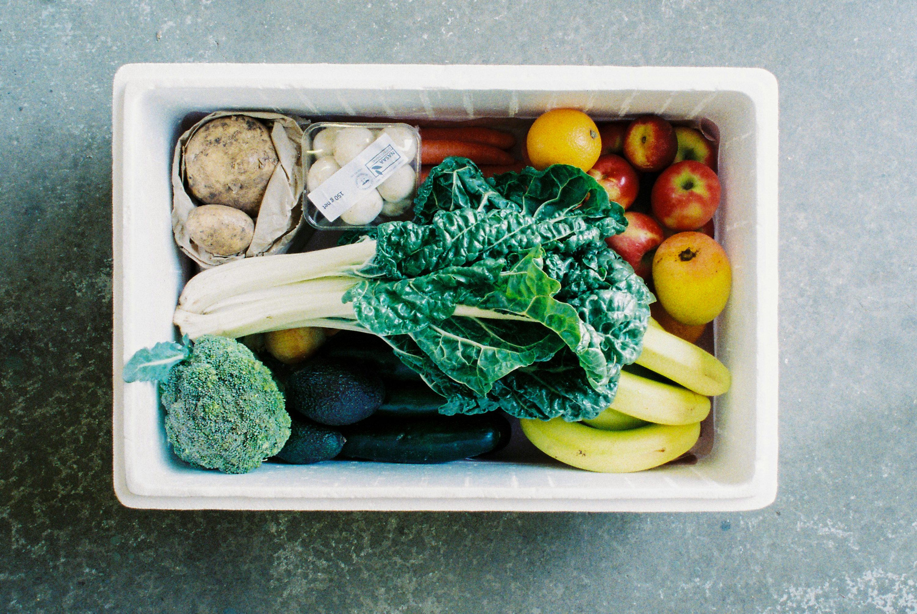 An overhead view of a grocery box filled with vegetables and fruit.